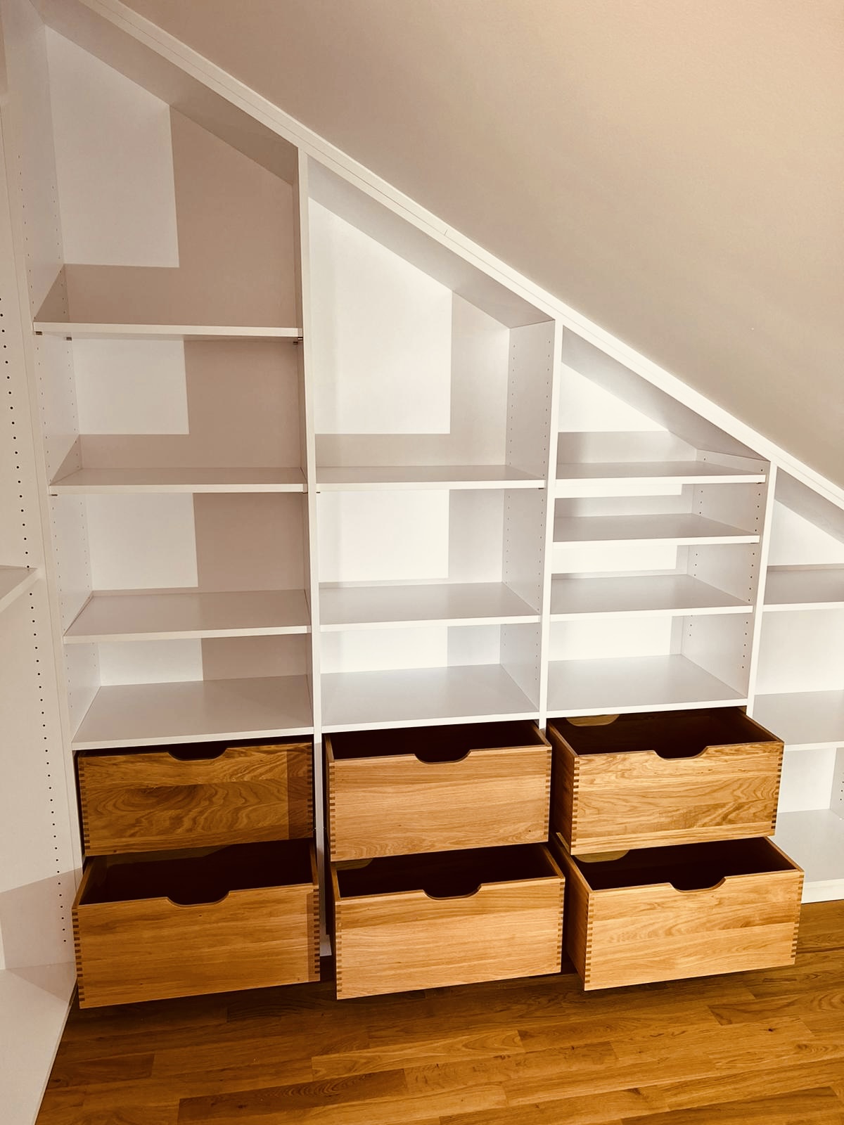 Einbauschrank unter Dachschräge im begehbaren Kleiderschrank: Weiße Regalböden und Schubladen aus Massivholz.